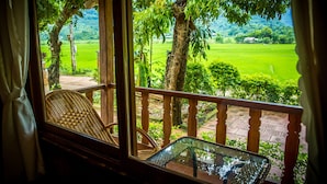 A balcony with wicker chairs and a glass table, overlooking a lush green landscape with trees and a clear sky. - Mai Chau Sunrise Village (Mai Chau)