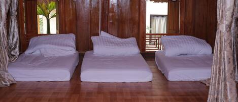 Habitación con tres camas individuales, suelo de madera y vistas a palmeras a través de las ventanas.