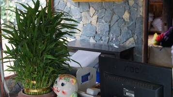 Un mostrador de recepción con un letrero que dice "RECEPTION", una computadora, una planta en maceta y una figura decorativa de cerámica.