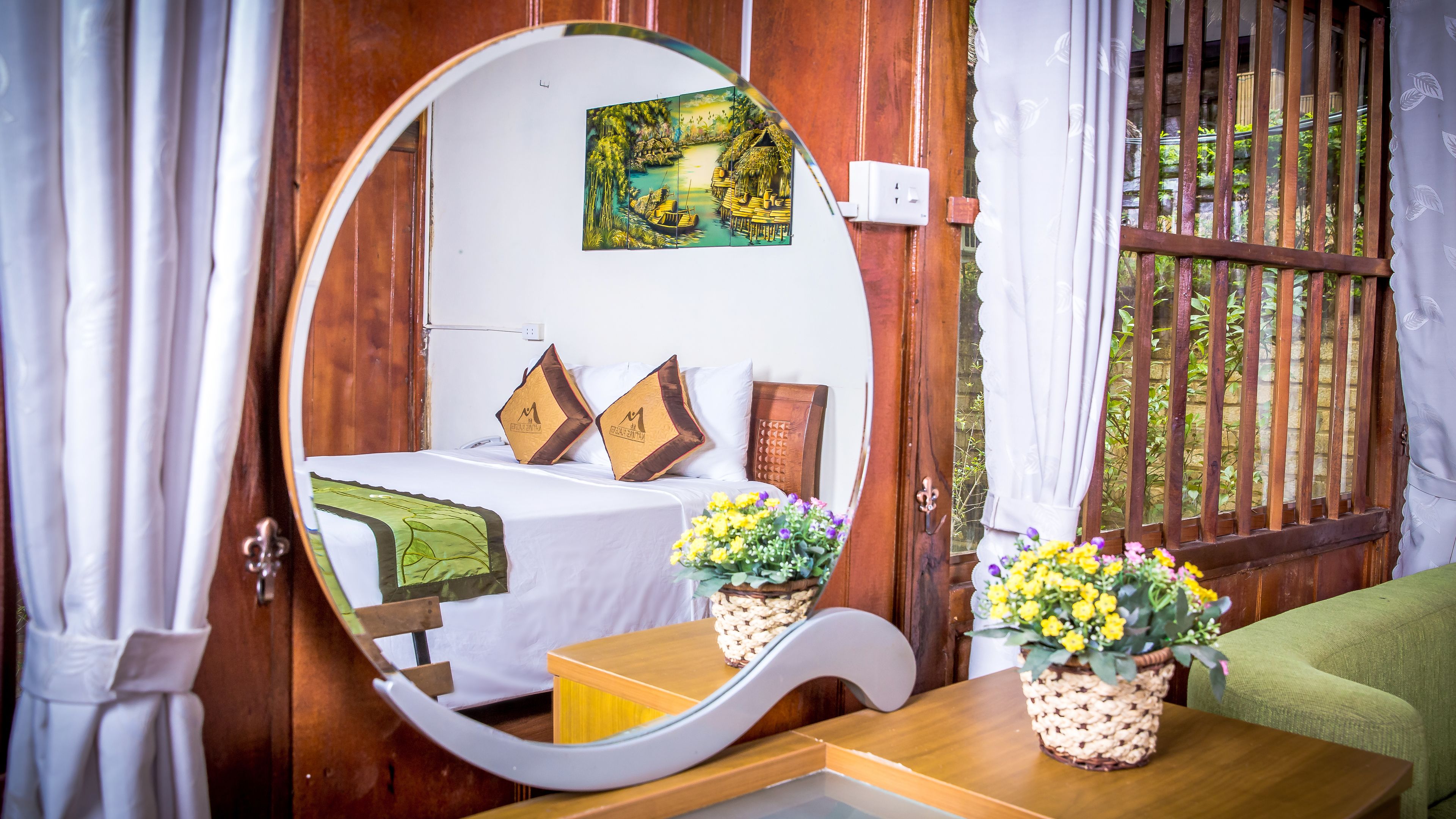 A wooden room with a bed, a mirror, and two flower vases on a table.