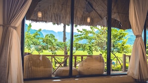 A covered outdoor seating area with wicker furniture and a view of a green landscape with trees and mountains. - Mai Chau Sunrise Village (Mai Chau)