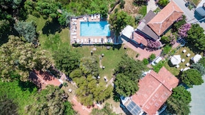 Eine Luftaufnahme eines Grundstücks mit Swimmingpool, Liegestühlen, Garten und einem Gebäude mit rotem Dach.