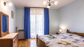 Ein Schlafzimmer mit einem hölzernen Bett, einem Schminktisch, einem Nachttisch, einem Fenster mit blauen Vorhängen und einer Heizung.