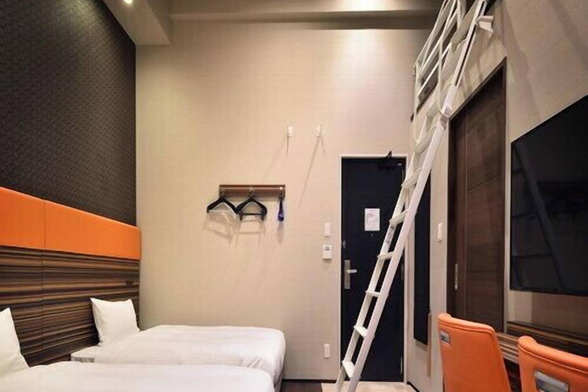 Une chambre d’hôtel avec deux lits, un bureau, une chaise, une télévision et une échelle.