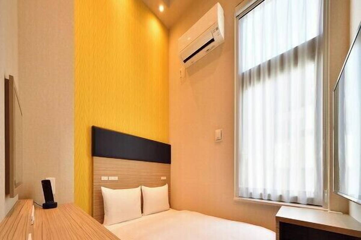 Une chambre d’hôtel équipée d’un lit, d’un bureau, d’une chaise, d’un appareil de climatisation et d’une fenêtre avec des rideaux.