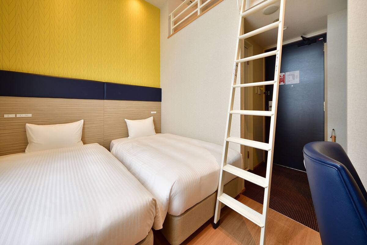 Une chambre d’hôtel avec deux lits, une échelle, un bureau et une porte.
