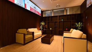 A hotel lobby with a modern design, featuring sofas, a coffee table, and a large digital display.
