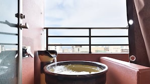 A hot tub with water flowing into it, a window with a view of buildings, and a door with a handle. - Hotel WBF Grande Hakata (Fukuoka)