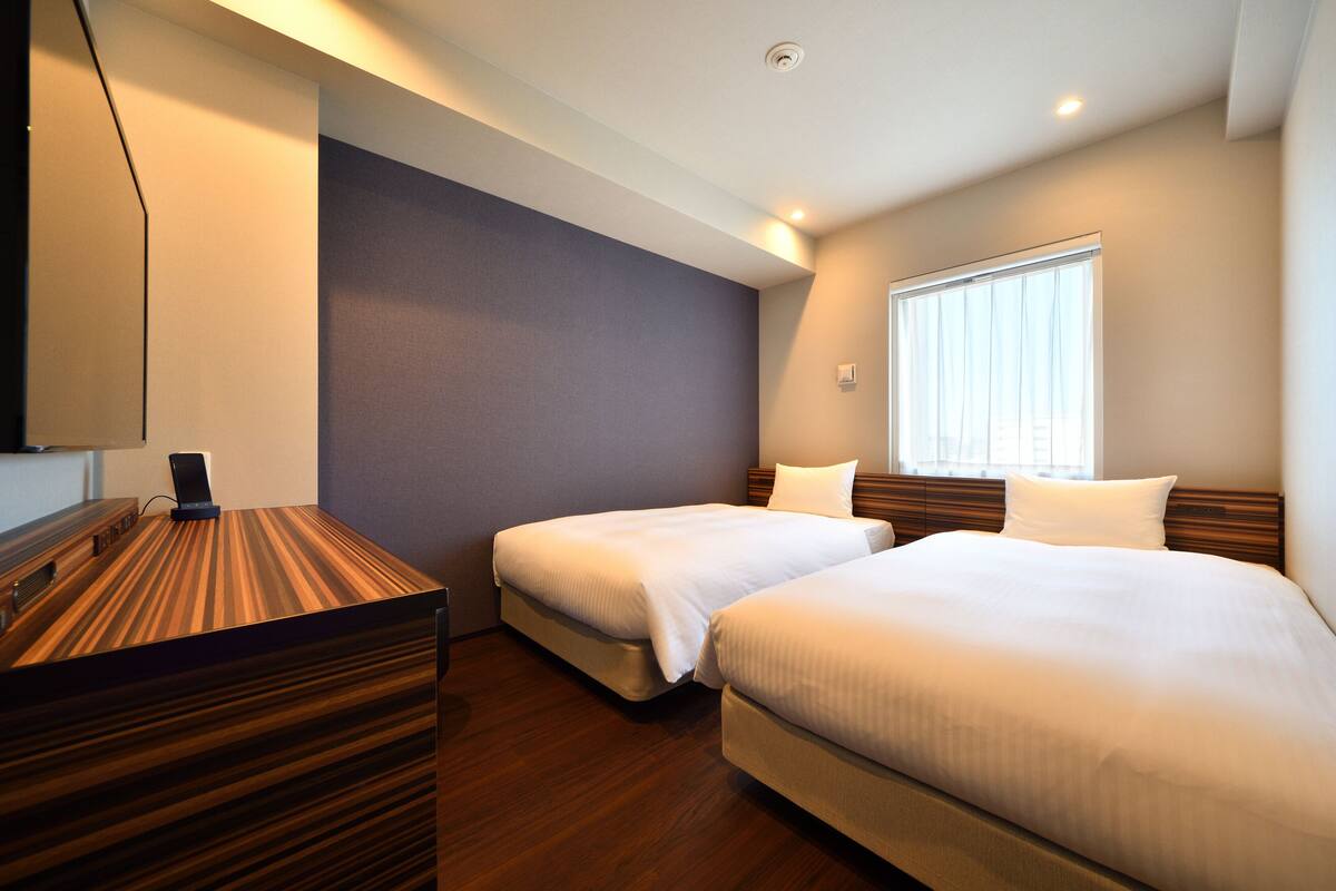Une chambre d’hôtel avec deux lits, un bureau et une fenêtre.