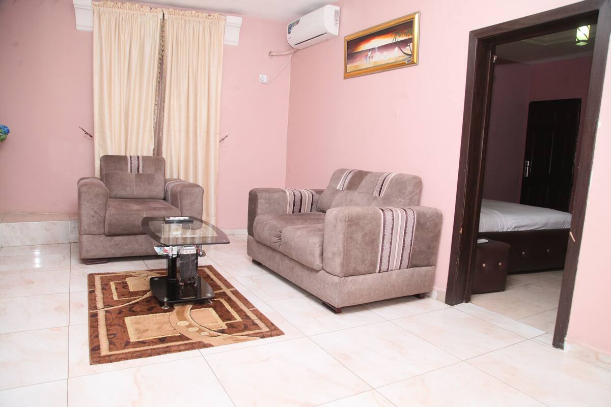 A living room with two sofas, a coffee table, and a bed in the adjacent room.