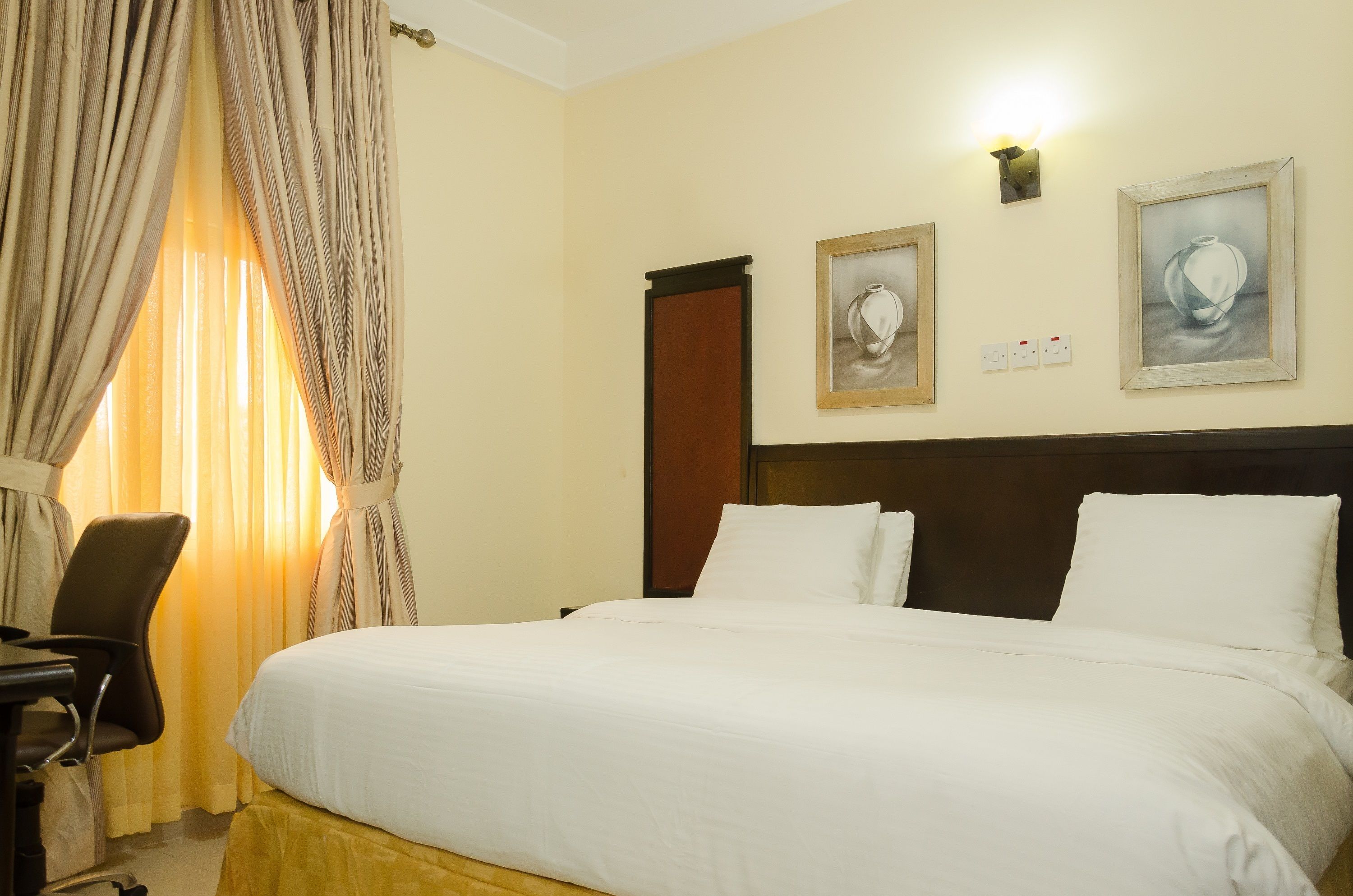 Ein Hotelzimmer mit einem Bett, einem Schreibtisch und zwei gerahmten Kunstwerken an der Wand.