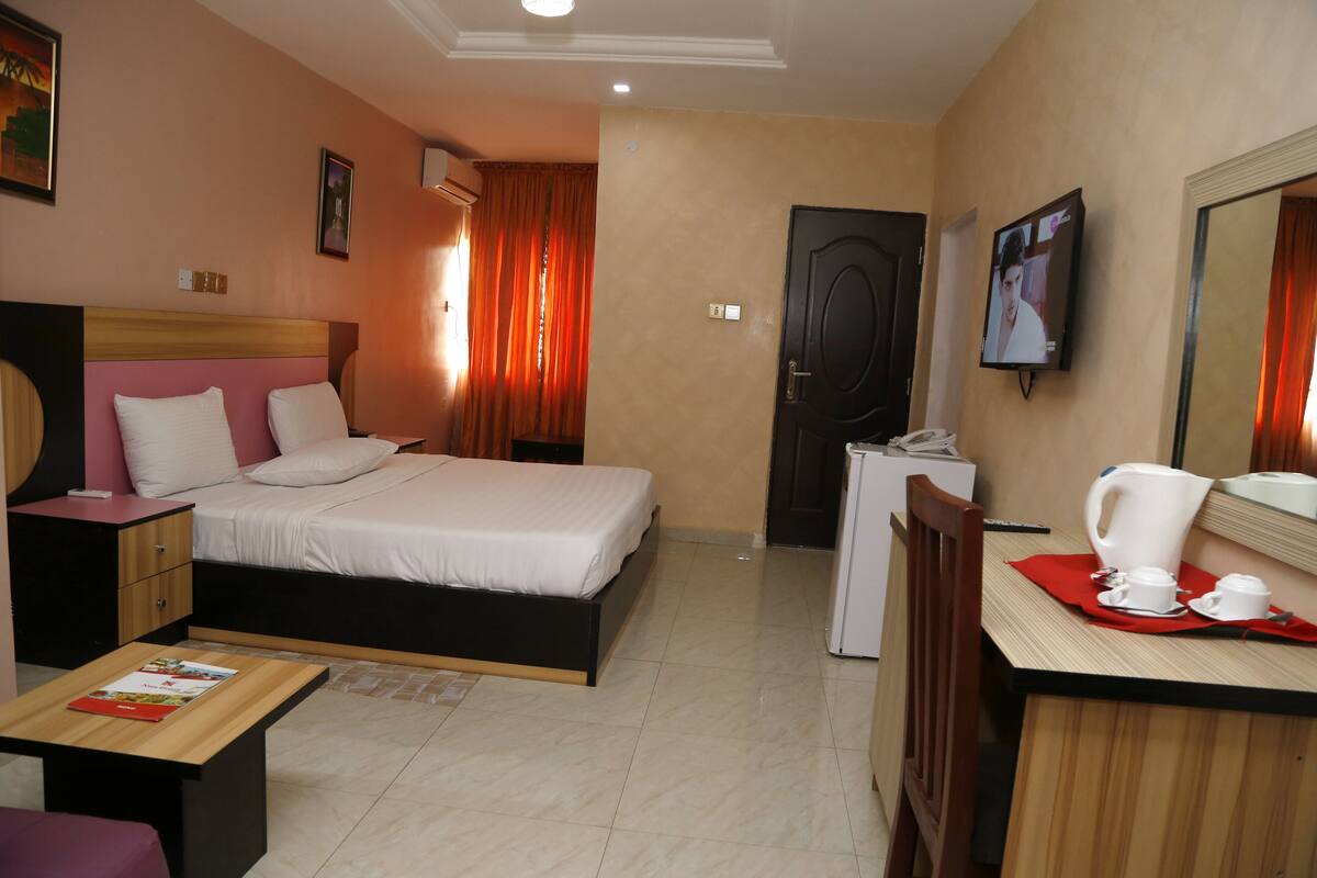 A hotel room with a bed, bedside table, desk with a chair, and a television.