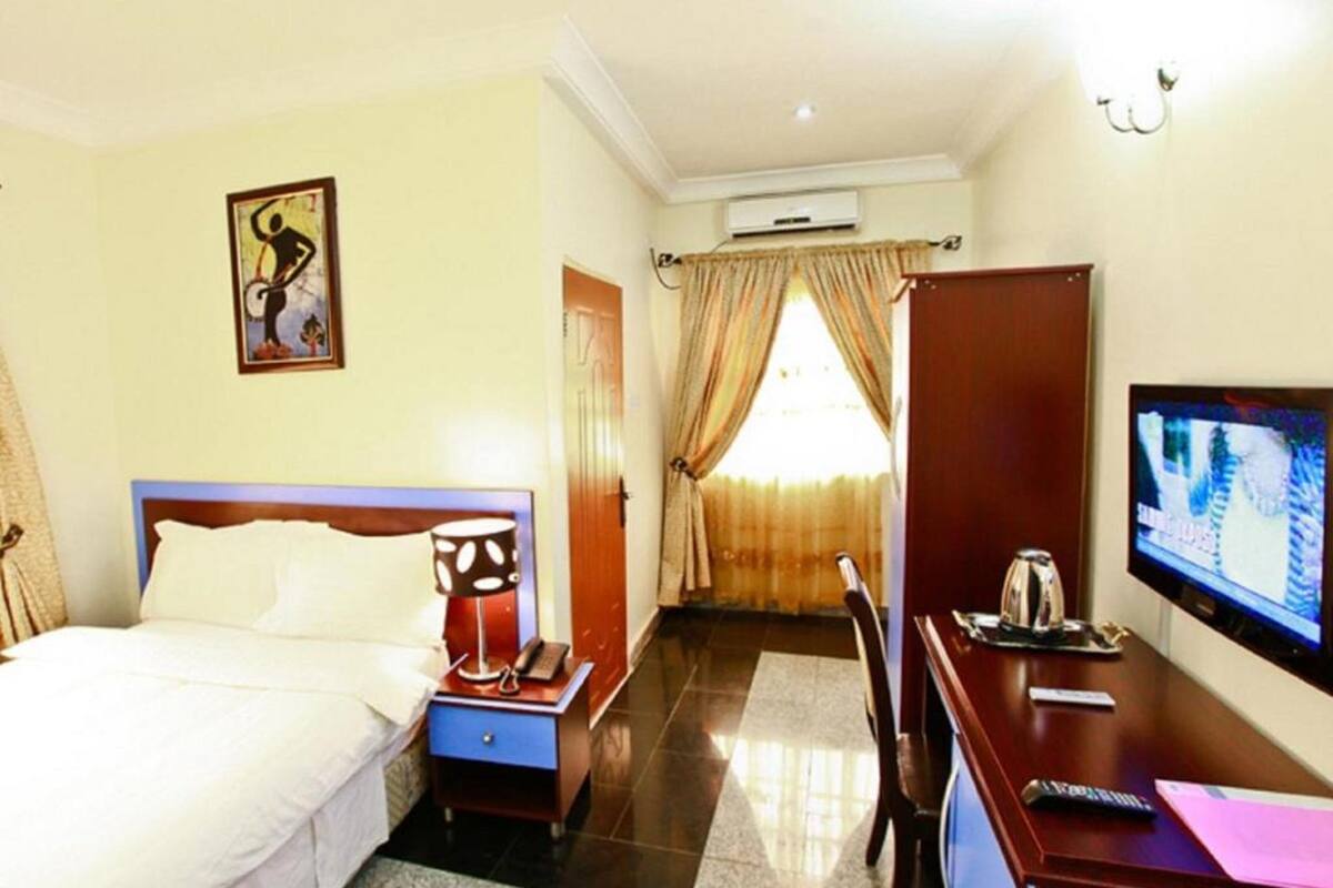 A hotel room with a bed, bedside table, lamp, TV, desk, chair, and curtains.