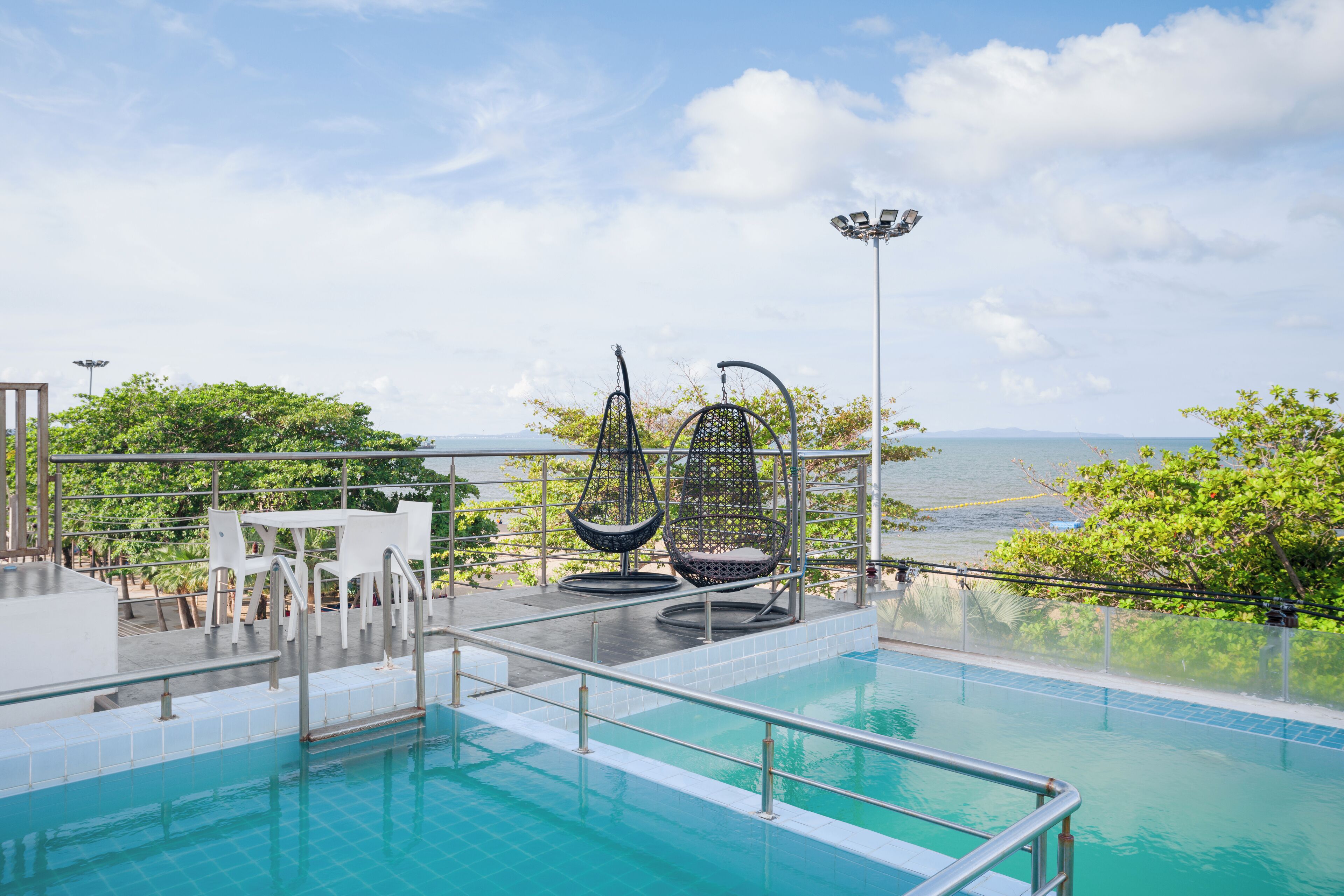 Uma área de piscina com vista para o oceano, cadeiras brancas e redes suspensas.