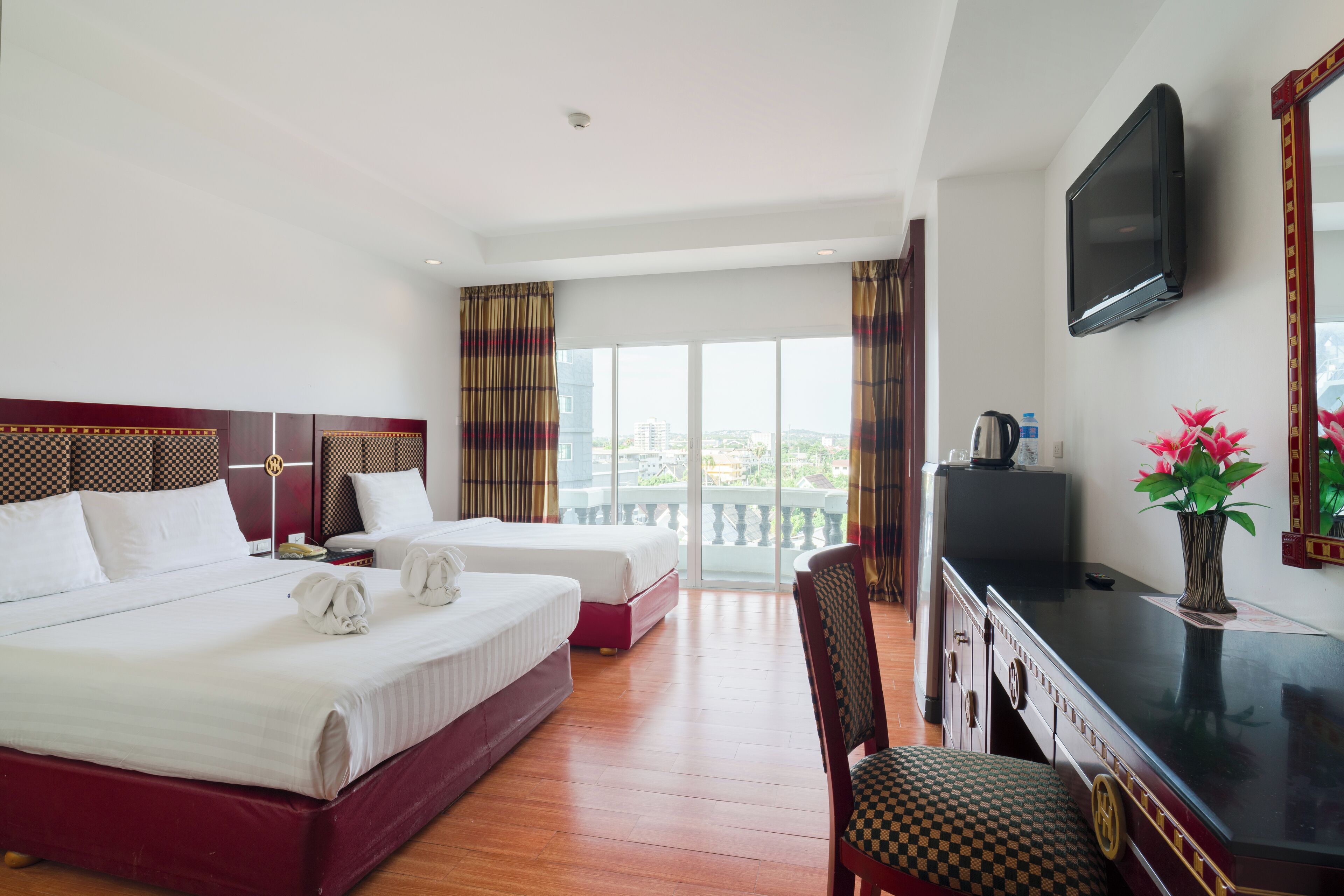 Habitación de hotel con dos camas, un escritorio, una silla, un televisor y un balcón con vistas.