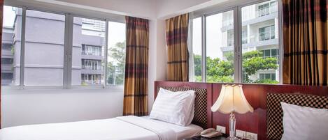 A hotel room with two beds, a nightstand with a lamp, and a window with curtains.