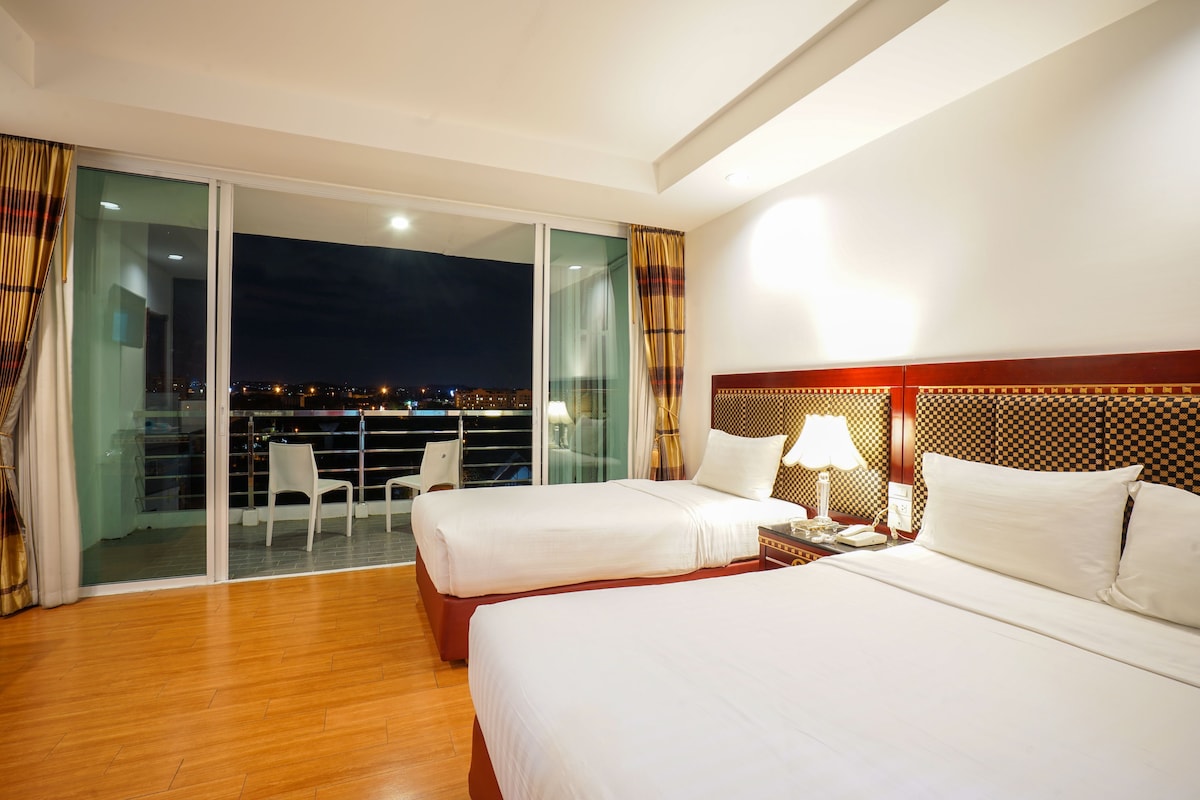Ein Hotelzimmer mit zwei Betten, einem Balkon mit einem Stuhl und Blick auf die Stadt bei Nacht.