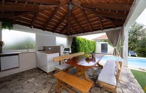 An outdoor kitchen with a stone floor, a wooden table with benches, a sink, and a gas stove.