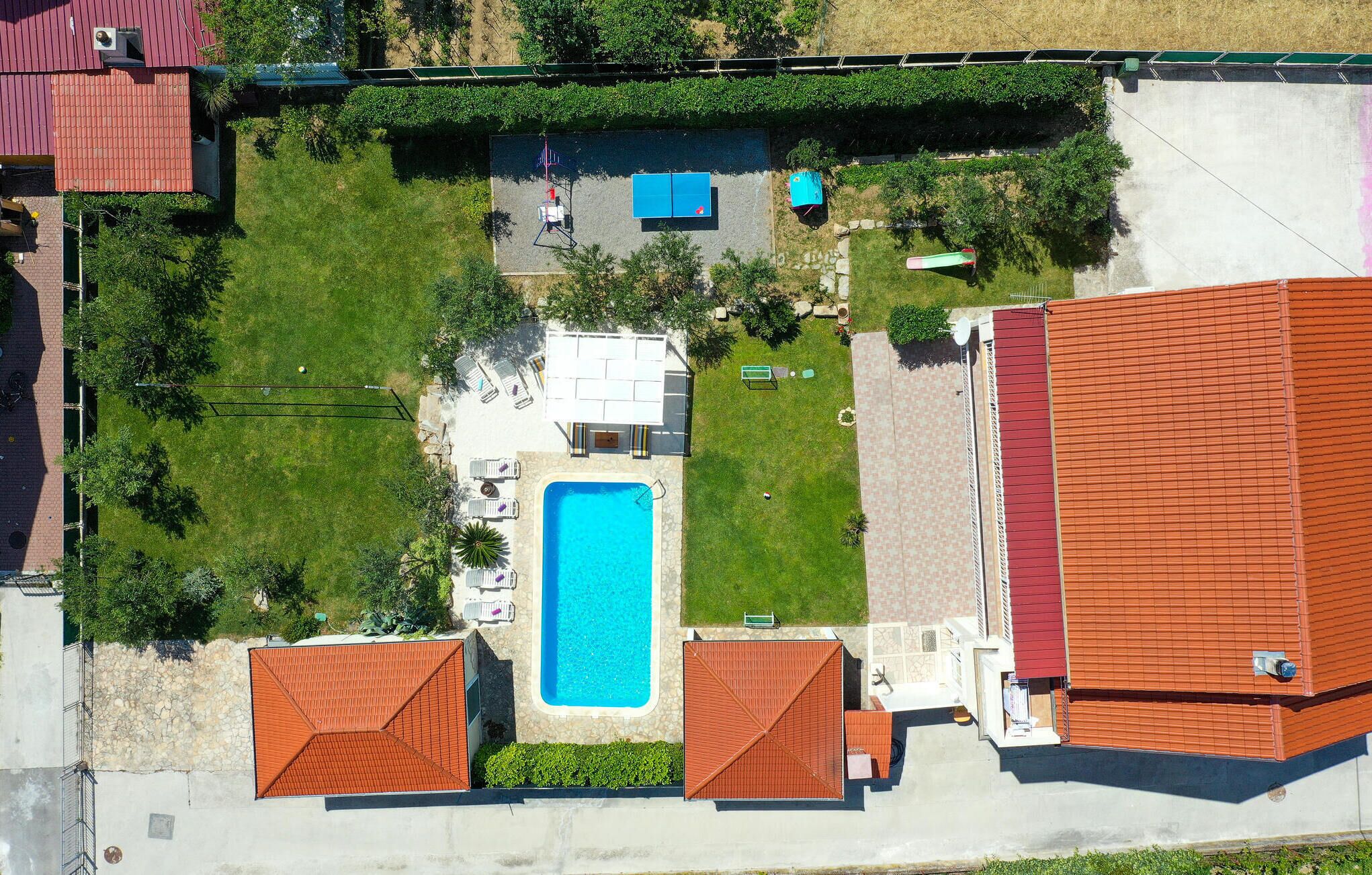 Vista aérea de una propiedad con piscina, tumbonas y cancha de tenis.