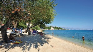 A beach with people sunbathing and swimming, picnic tables, and a clear view of the sea. - Nice home in Kastel Luksic with sauna (Kastel Luksic)