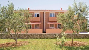 Un bâtiment à deux étages, avec un mur de pierre à l’avant, entouré de pelouse et d’arbres.