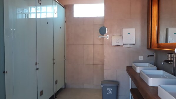 A bathroom with a row of lockers, a hand dryer, a trash bin, and a sink with a mirror above it. - M Boutique Hostel Legian (Kuta)