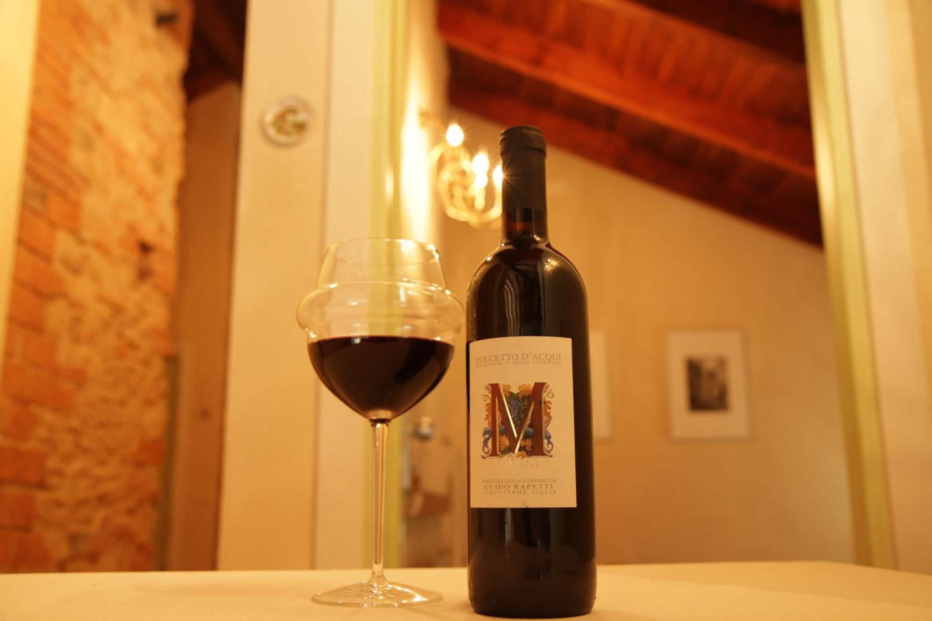 Una bottiglia di vino e un bicchiere su un tavolo in una stanza con parete in mattoni e soffitto in legno.
