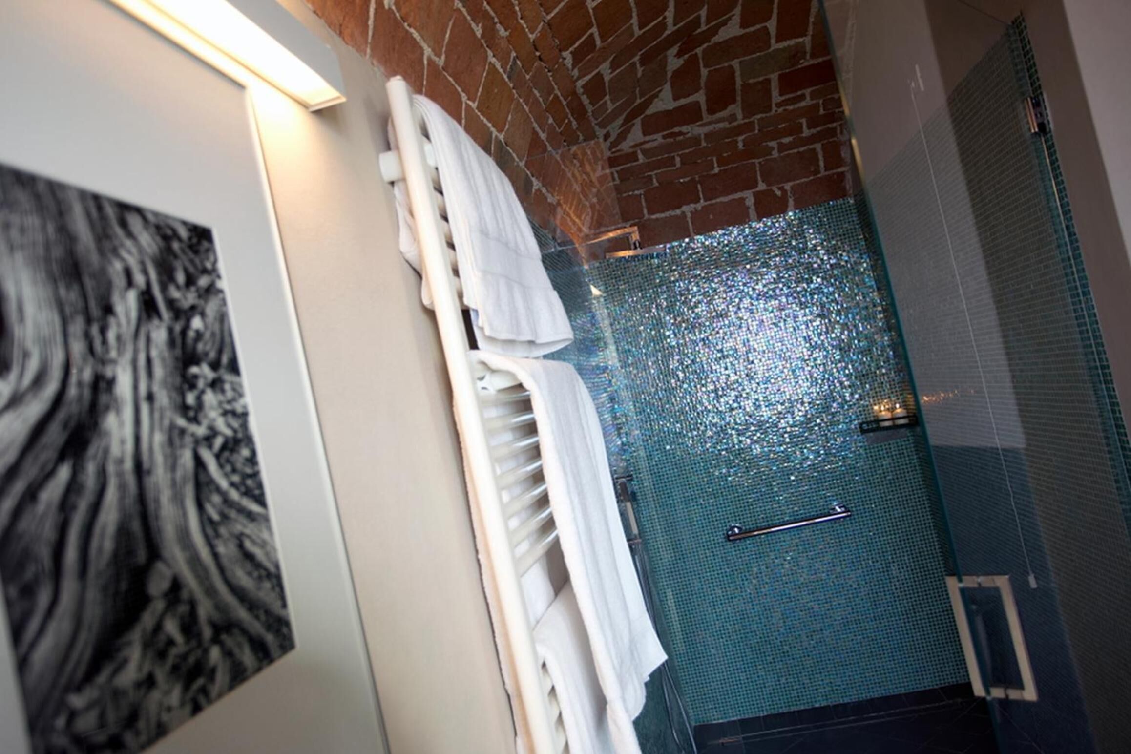 A bathroom with a tiled shower, a towel rack, and a wall-mounted towel.