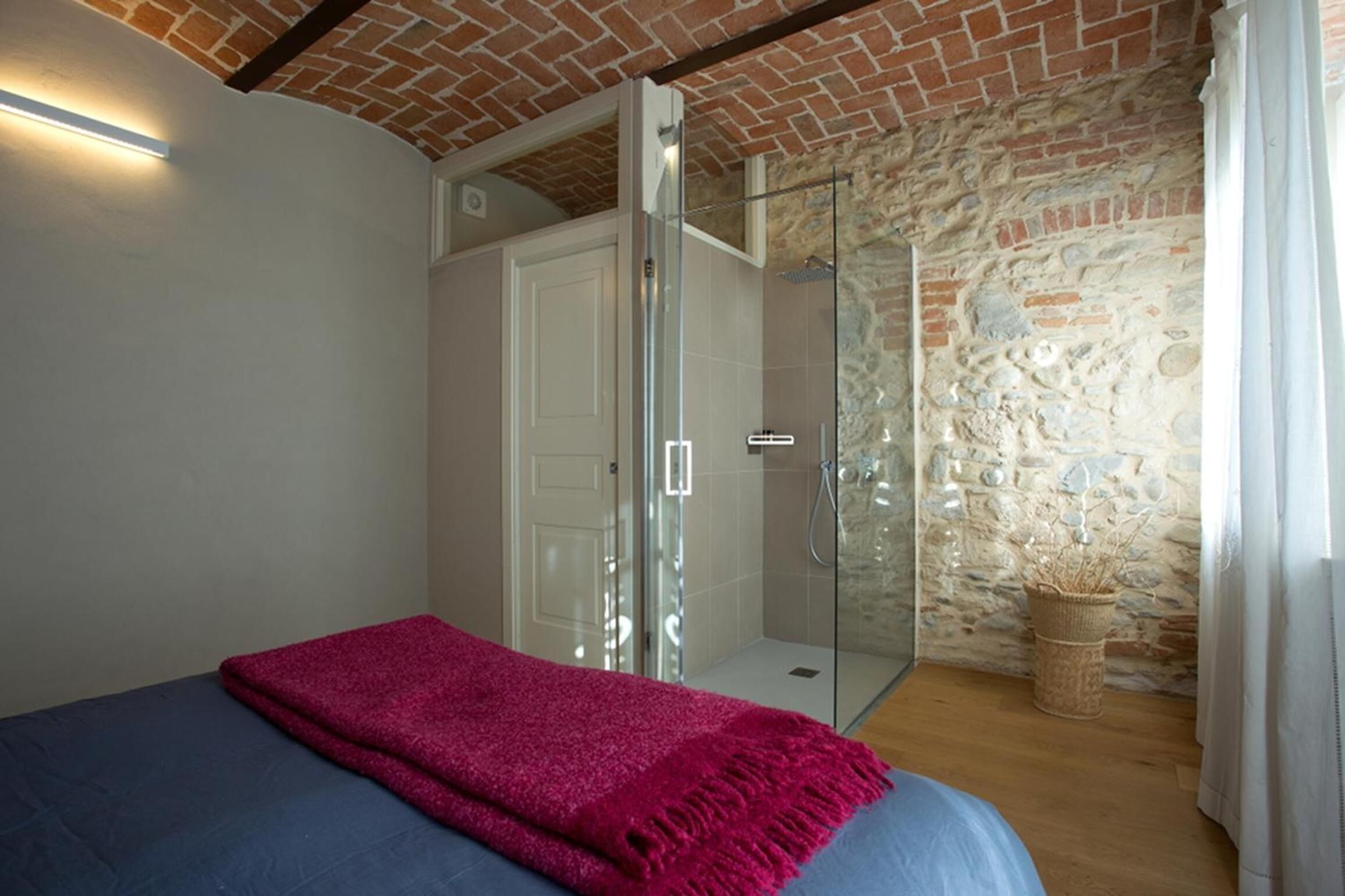Une chambre à coucher avec un lit, une douche en verre, un mur en pierre et une porte blanche.