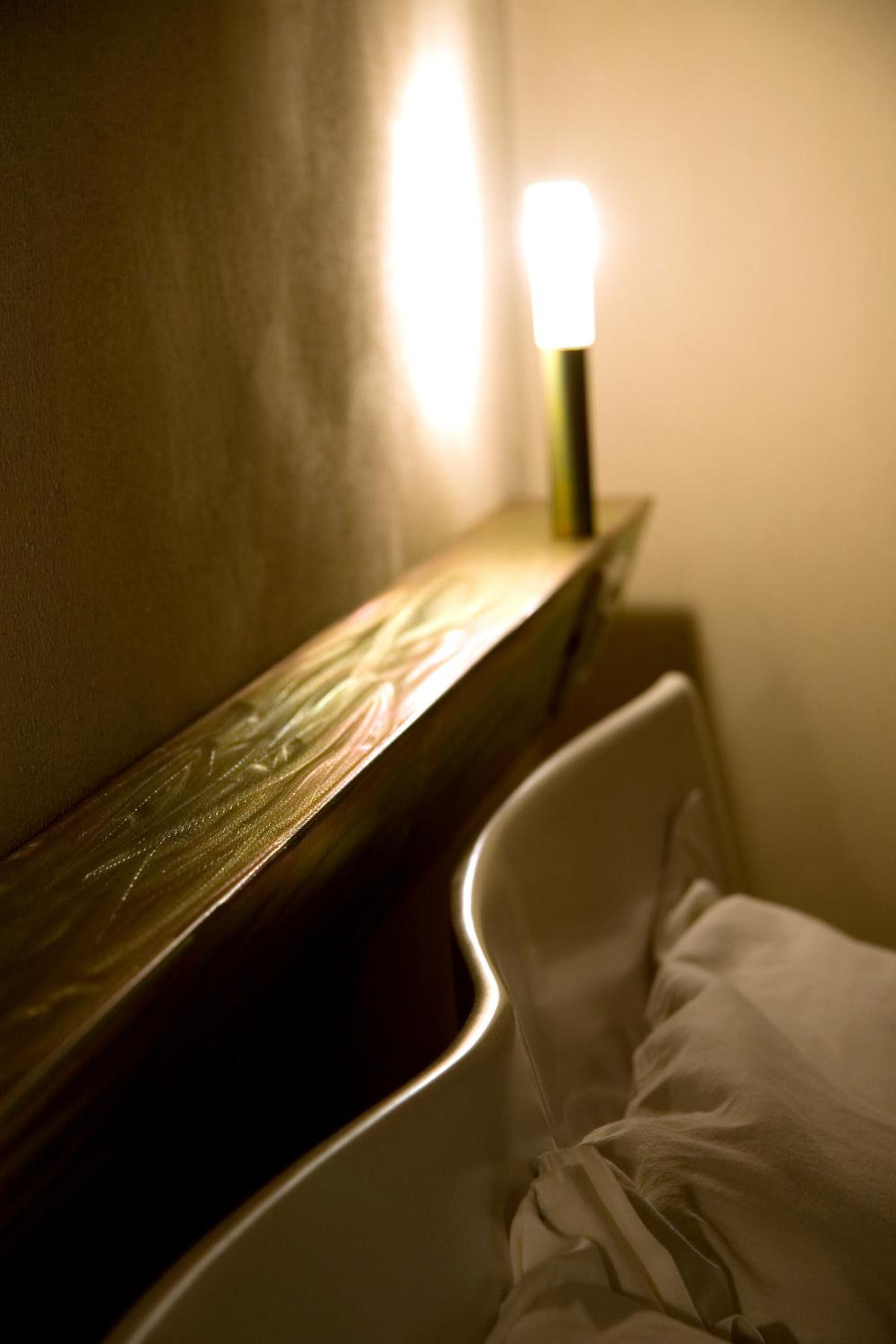 A hotel room with a bed, a bedside table, and a wall-mounted light.