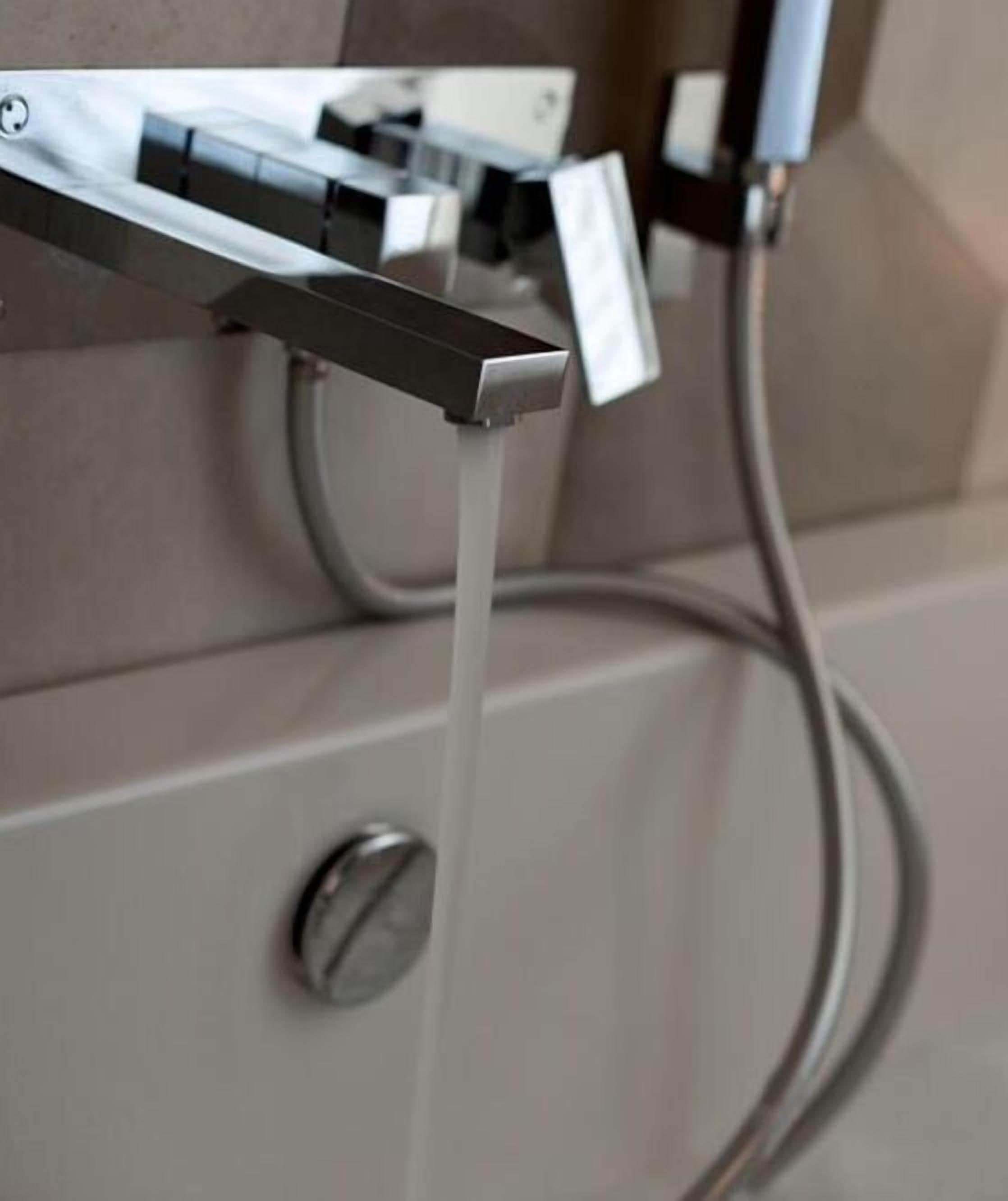 Un baño moderno con un grifo de pared y una manguera de agua visible.