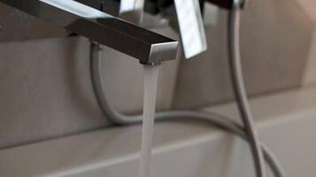 Un baño moderno con un grifo de pared y una manguera de agua visible.