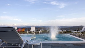 Una piscina en la azotea con sillas de descanso y una fuente, con vistas a un paisaje montañoso.