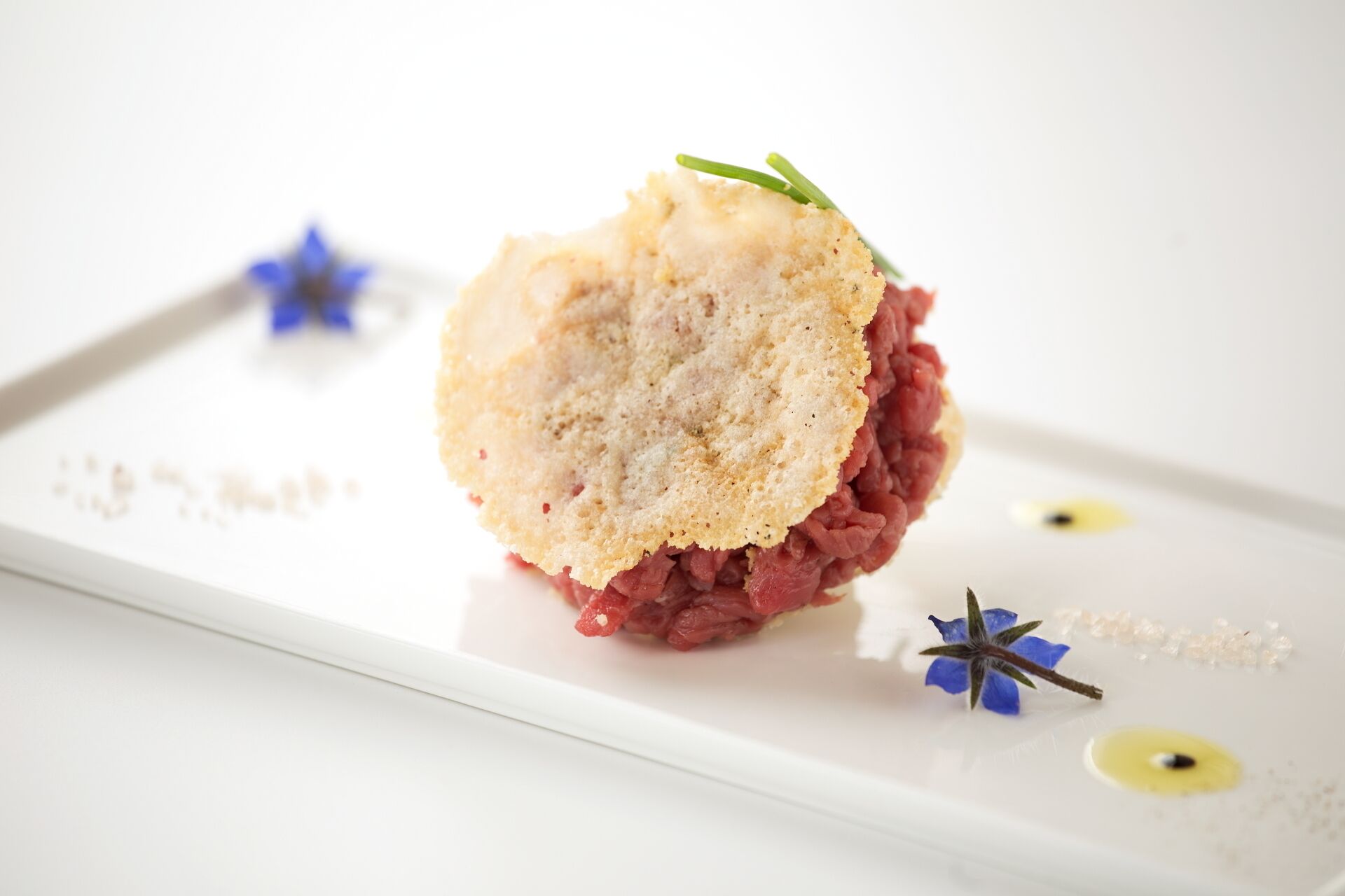Un postre con una cobertura similar a pan, sobre un plato blanco, decorado con una ramita de flores verdes y azules.