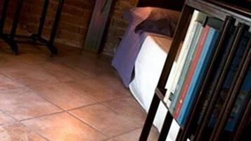 Una habitación con pared de ladrillo, una cama con cabecera blanca, una mesita de noche y una estantería llena de libros.