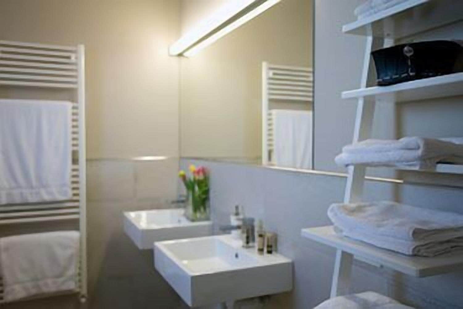 A modern bathroom with two sinks, a mirror, and shelves with folded towels.