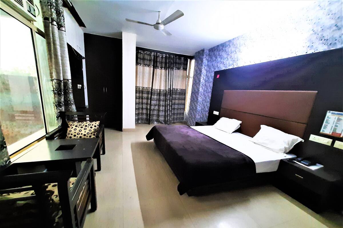 A hotel room with a bed, a desk, a chair, a ceiling fan, and a window with curtains.