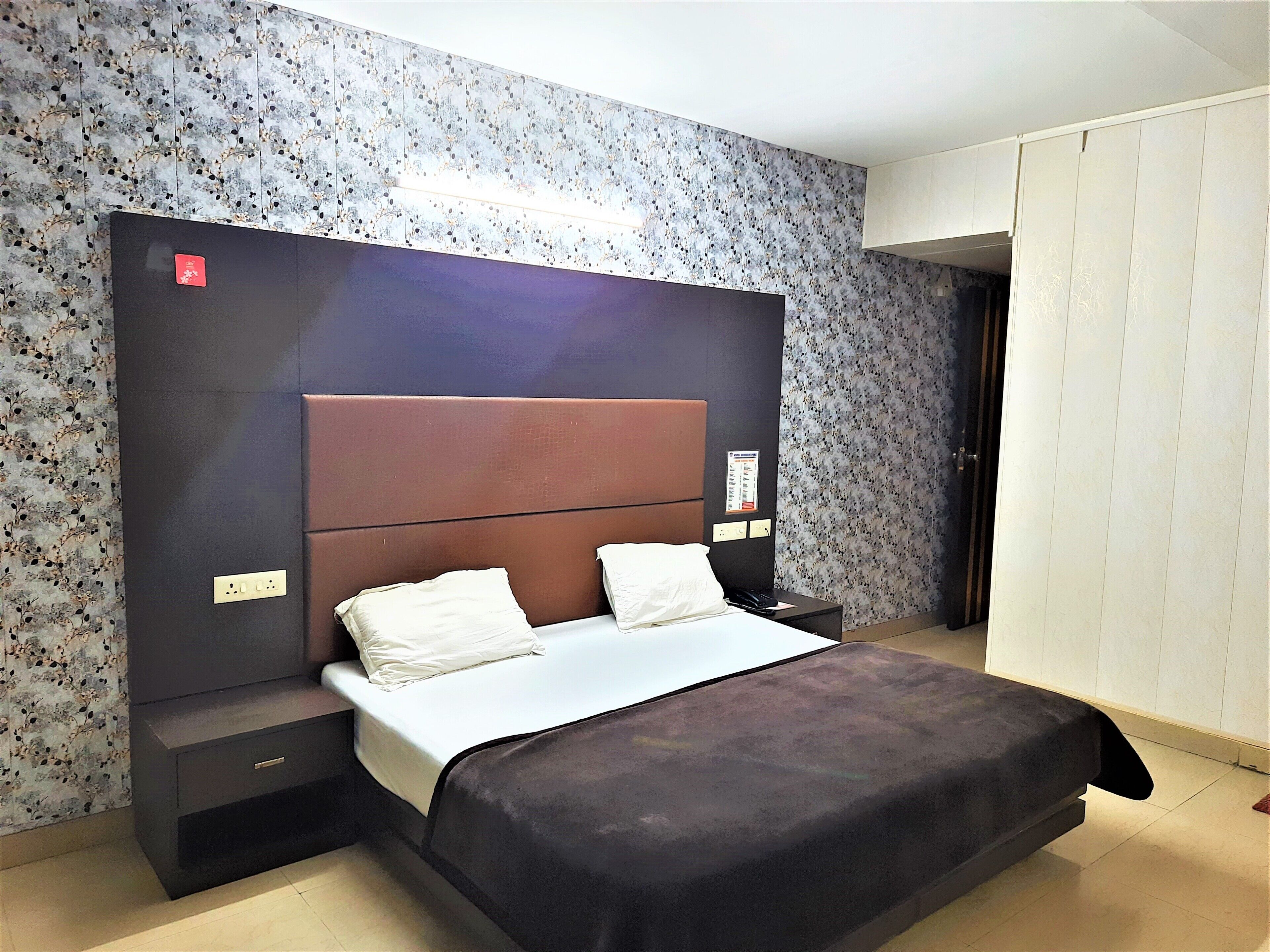 Un dormitorio moderno con una cama grande, cabecera oscura y un papel tapiz con estampado floral.
