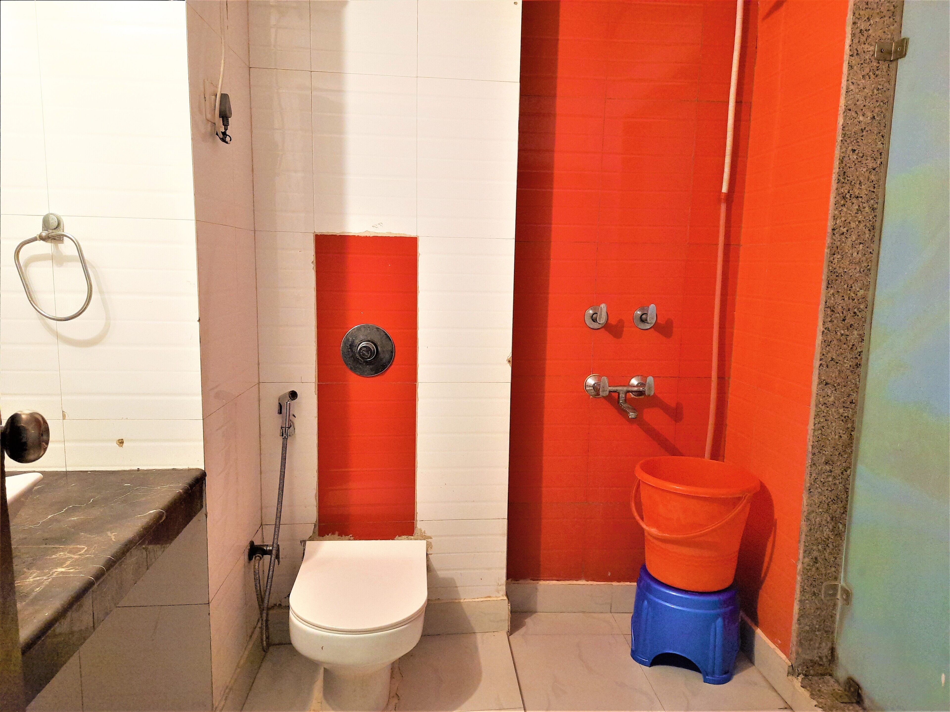 Un baño con inodoro blanco, cabina de ducha roja y taburete azul.