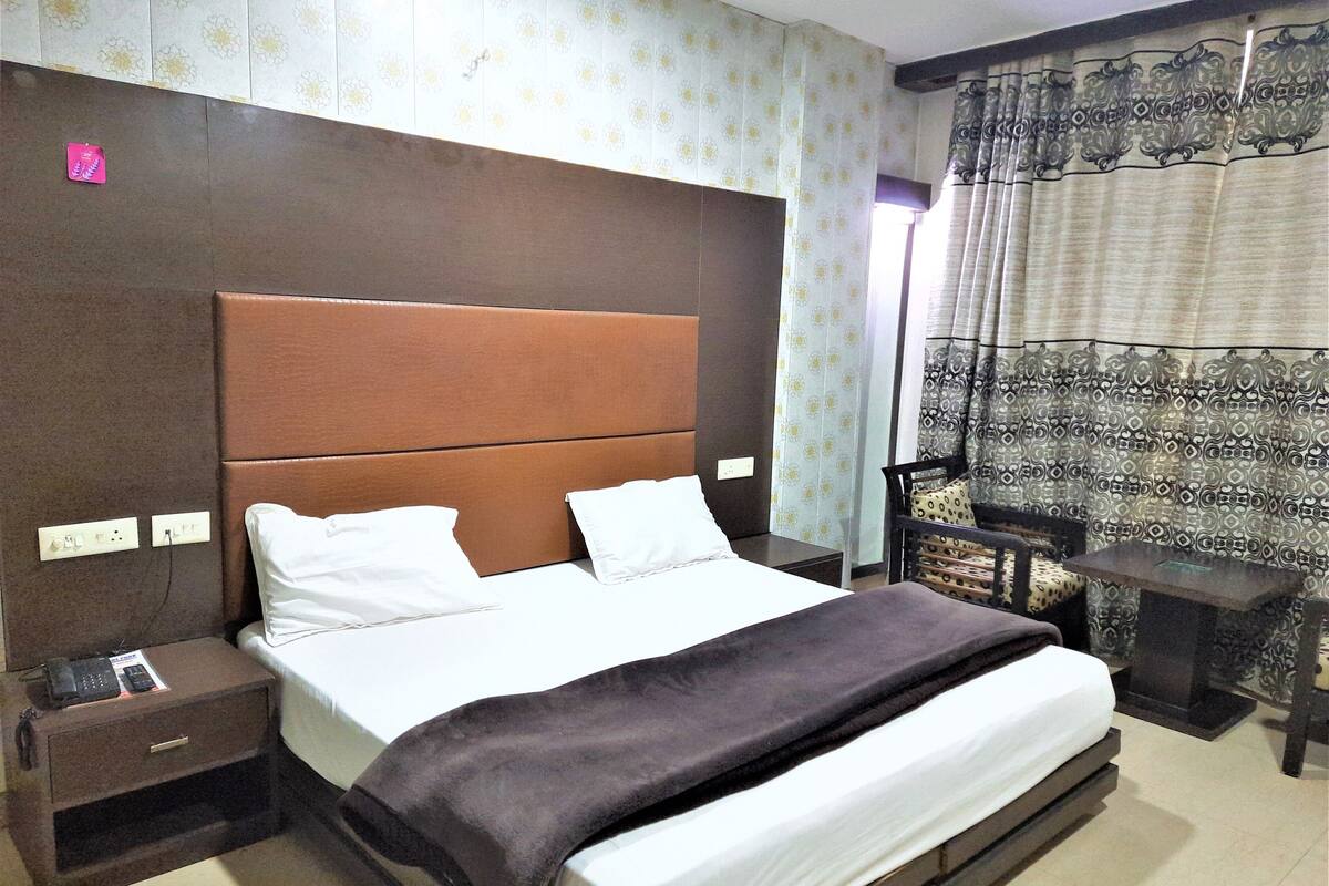 A hotel room with a large bed, a nightstand, a bedside table, a lamp, and a window with curtains.