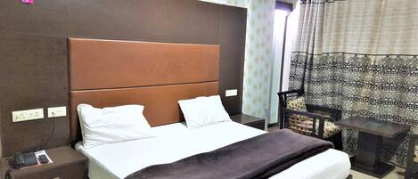 A hotel room with a large bed, a nightstand, a bedside table, a lamp, and a window with curtains.