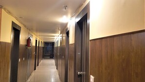 Un long couloir étroit aux murs et aux portes recouverts de lambris en bois, qui mène à des pièces individuelles.