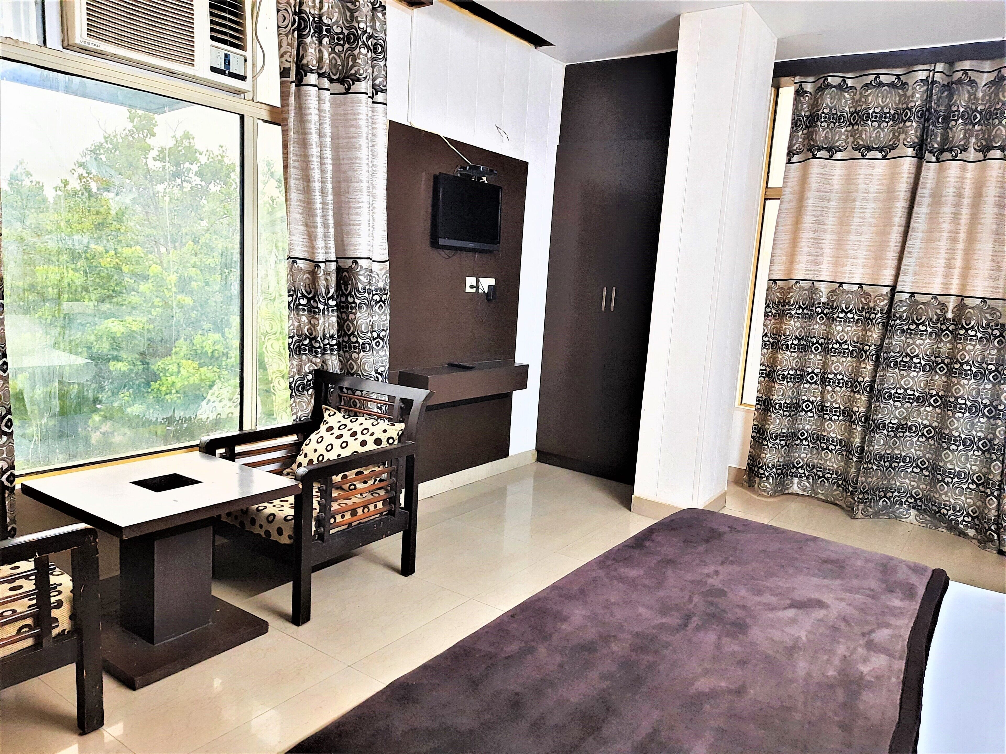 A modern room with a desk, chair, and a large window offering a view of greenery.