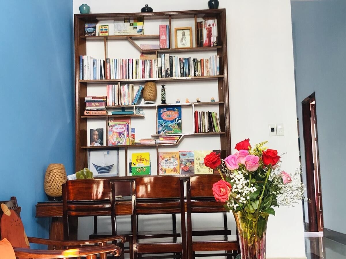 A room with a bookshelf filled with books, a wooden chair, a table, and a vase with flowers.
