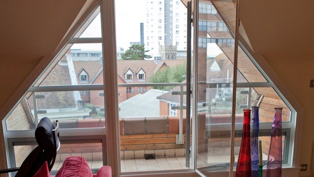 A room with a red couch, a glass door leading to a balcony, and a table with a decorative item. - Toothbrush Apartments - Central Ipswich (Ipswich)