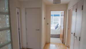 A hallway with wooden flooring, white doors, and a view into a bedroom with a bed and a window. - Toothbrush Apartments - Central Ipswich (Ipswich)