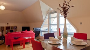 A modern loft apartment with a dining area, red furniture, and a large window offering a view. - Toothbrush Apartments - Central Ipswich (Ipswich)