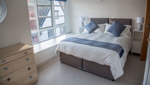 A bedroom with a bed, bedside tables, a dresser, and a window with blinds. - Toothbrush Apartments - Central Ipswich (Ipswich)