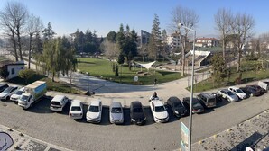 Un estacionamiento con varios autos y un camión, rodeado de árboles y edificios.