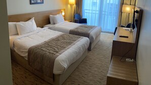 Habitación de hotel con dos camas, un escritorio, una silla, una lámpara y un cuadro en la pared.